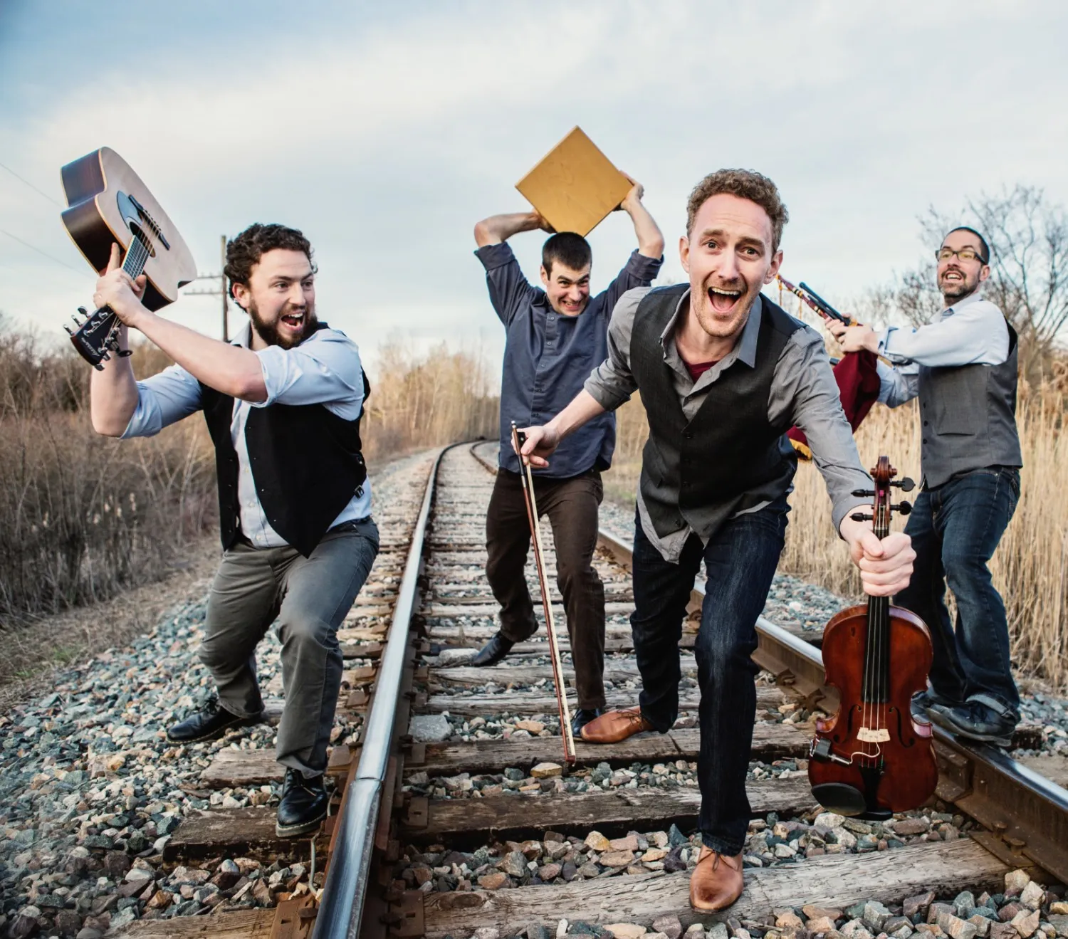Hunt the Hare striding down a railway track with guitar, fiddle, bow and cajón.